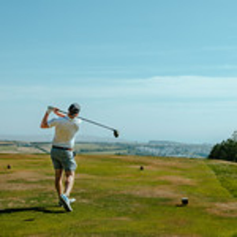 Man swinging golf club with scenic view.