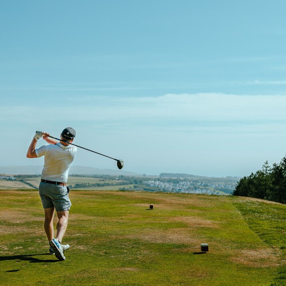 Man swinging golf club with scenic view.