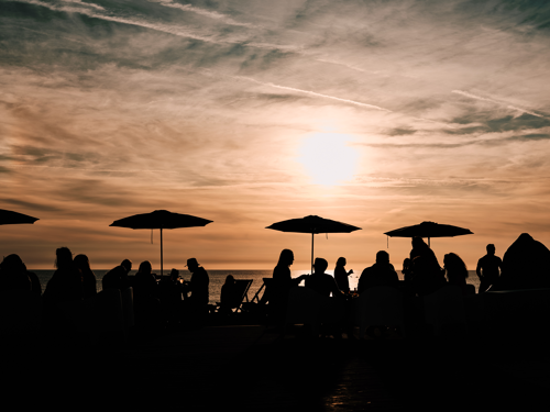 Silhouette of people eating at a beach restaurant with the sun setting behind them.